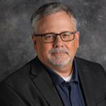 Tom Rank, Associate Professor for the Religion Department, against grey background.