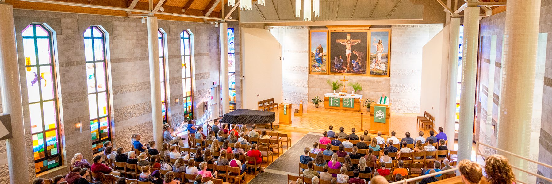Bethany Lutheran College students sit in wooden chairs facing the altar in a church adorned with stained glass windows and religious artwork.
