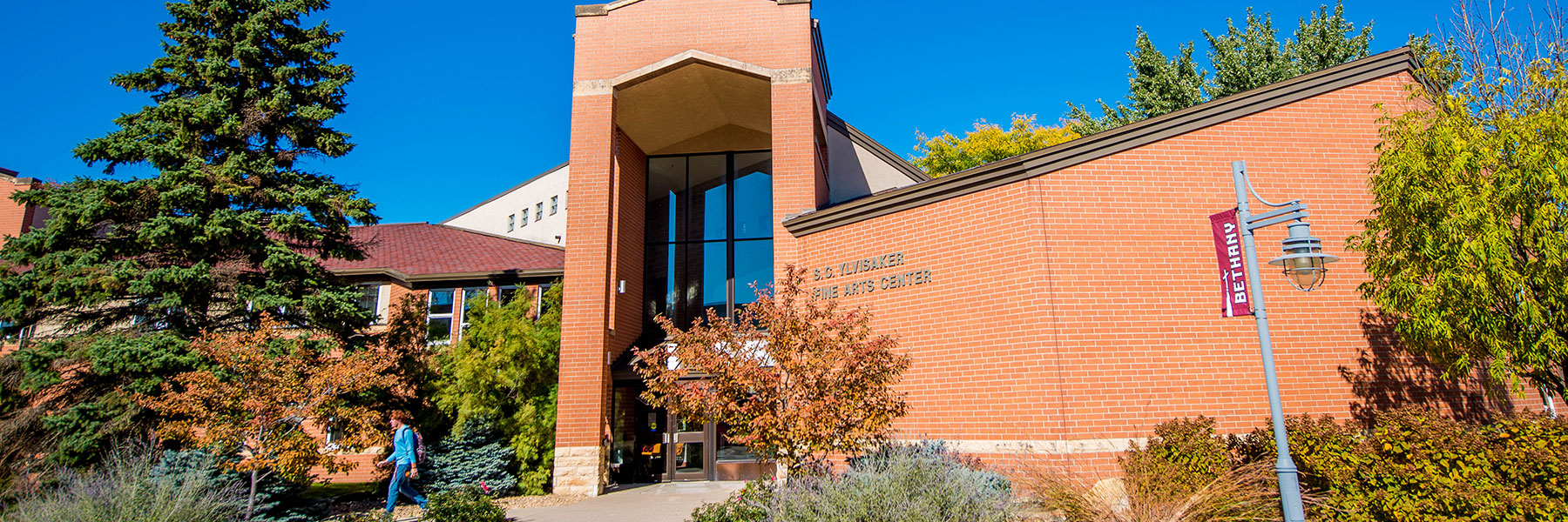 A brick university building with large windows at Bethany Lutheran College, surrounded by trees and set against a clear blue sky.