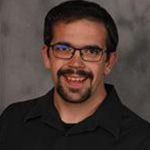 Zay Koepsell, Assistant Professor for the Business Administration Department and Instructor for the Business Administration Department, with a gray backdrop.