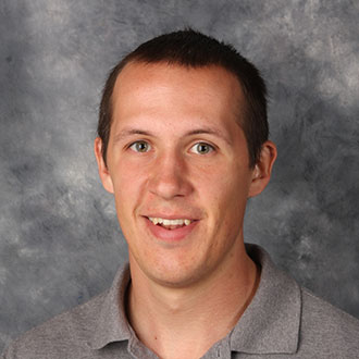 Scott Abbey, Information Technology Professional for the Information Technology Services Department, poses in front of a gray textured background.