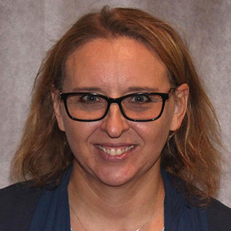 Sue Beavis, Adjunct Faculty for the Nursing Department, smiles at the camera in front of a gray background.