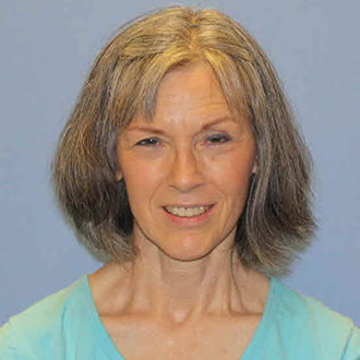 A middle-aged woman with short gray hair, wearing a light blue top, smiles slightly against a plain blue background.