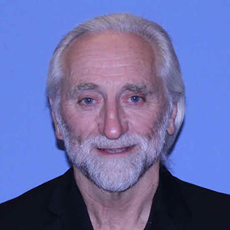 Dan Birkholz, Adjunct Faculty for the Legal Studies Department, smiles in front of a plain blue background.