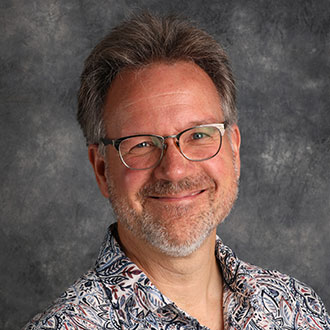 Peter Bloedel, Professor for the Theatre Department, in front of a gray mottled background.