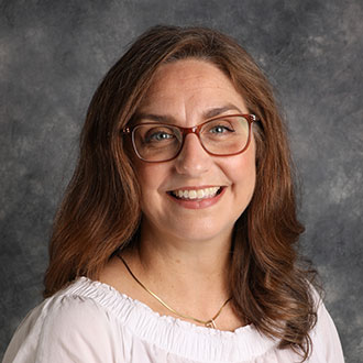 Sarah Bloedel, Data Entry and Office Assistant for the Education Department, smiles in front of a gray mottled background.