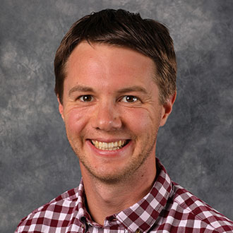 Ryan Bolte, Associate Dean of Students for the Student Affairs Department and Assistant Coach Men's Soccer for Athletics Department, stands in front of a gray mottled background.