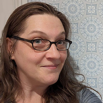 Charis Carmichael Braun, Adjunct Faculty of Fine Arts for the Media Arts Department, in front of a blue and white patterned wall.