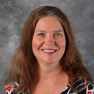 Cheryl Clendenin, Assistant Professor for the Nursing Department, stands in front of a gray textured background.