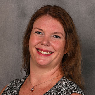 Karina Clennon, Assistant Professor for the Clinical Mental Health Counseling – Graduate Programs Department and Online Instructor for the Academic Affairs Department, smiling in front of a plain gray background.
