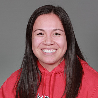 Angela Dabu, Head Softball Coach, wearing a red hoodie, smiles at the camera against a plain gray background.