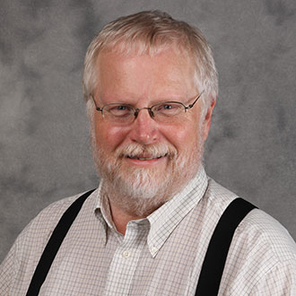 Mark DeGarmeaux, Professor for the Religion Department, standing against a grey backdrop.
