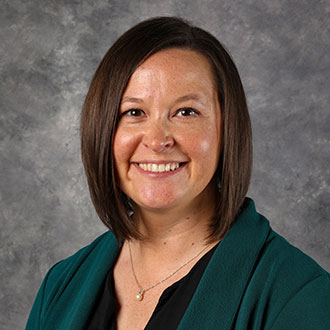 Jami DeVos, Office & Enrollment Coordinator of the Graduate Programs Department, standing against a gray background.