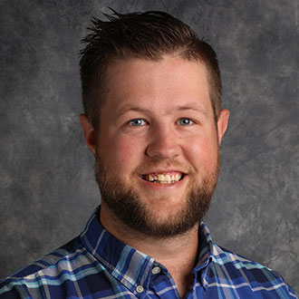 Lucas Dorton, Counselor for the Admissions Department, is positioned in front of a gray mottled background.