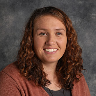 Brittany Espinoza, Assistant Professor for the Mathematics Department, smiles in front of a textured gray background.