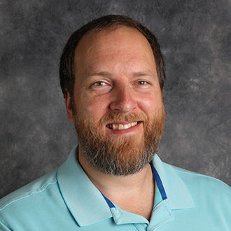 Ben Faugstad, Associate Professor for the Music Department, is posed against a gray background.