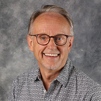 Craig Ferkenstad, Adjunct Faculty for the Religion Department, standing in front of a gray mottled background.