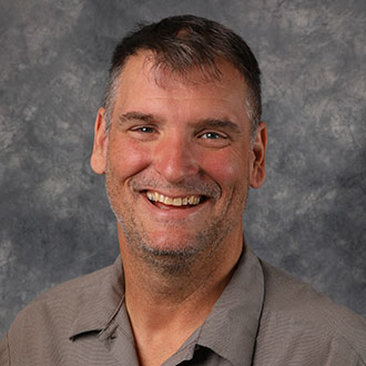 Mike Fletcher, Superintendent of Buildings Technician for the Maintenance Department, positioned against a gray mottled background.