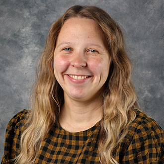 Emily Frank, Library Services Assistant for the Library Services Department, smiles in front of a gray mottled background.