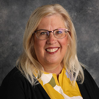Ann Fredrickson, Adjunct Faculty, Choraliers Director, Director of Handbells, and Mary Martha Singers Director for Music Department, poses against a gray studio backdrop.