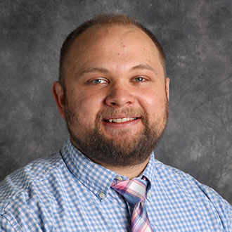 Lucas Fricke, Associate Professor for the Languages Department and Director of the Esports Department, poses in front of a gray backdrop.