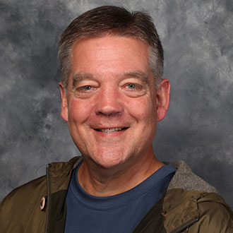 Jon Geistfeld, Accounts Payable Clerk for the Business Office Department, is posed in front of a gray mottled background.