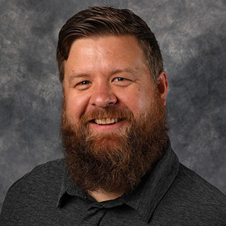 Dan Gerdts, Manager of the Spirit Store Department, sits in front of a gray textured background.