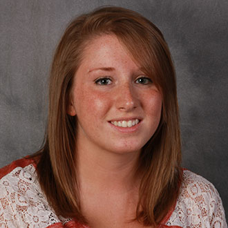 Alexis Gleason, Online Instructor for the Academic Affairs Department, smiles while posed against a gray backdrop.
