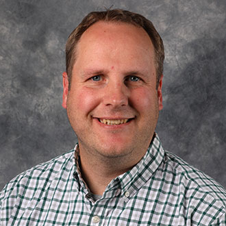 John Gunderson, Associate Professor for the Languages Department and Study Abroad Coordinator of the Academic Affairs Department, in front of a gray mottled background.