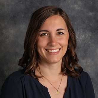 Stephanie Heidorn, Assistant Professor for the Media Arts Department, smiles in front of a gray mottled background.
