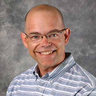 Chad Heins, Associate Professor for the Biology Department, in front of a gray mottled background.