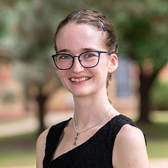 Emily Helmen, Adjunct Faculty for the English Department, smiles in front of a gray background.
