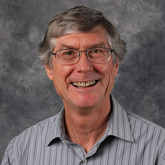 Doyle Holbird, Professor for the Biology Department, stands in front of a gray mottled background.
