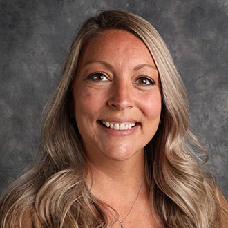 Katie Hopp, Visual Communication & Social Media Specialist for the Institutional Communication Department, stands in front of a gray studio background.