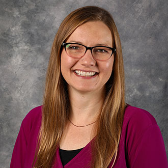 Alyssa Inniger, Director of the Library Services Department, smiles in front of a gray studio backdrop.