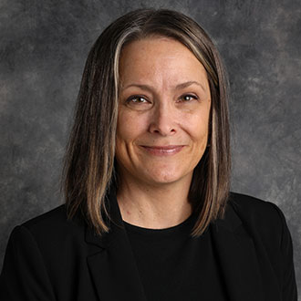 Angie Johnson, Associate Professor for the English Department and Writing Center Coordinator for the Academic Affairs Department, smiling in front of a mottled gray background.