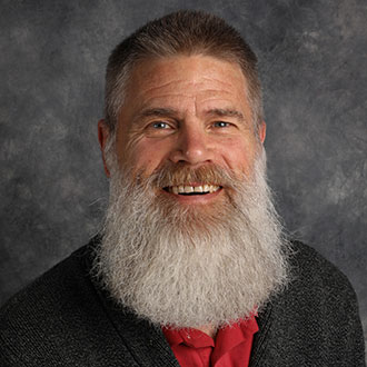 Lars Johnson, Professor for the English Department, is posed in front of a gray studio backdrop.