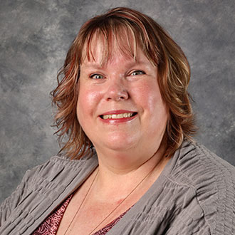 Angela Kelly, Technical Services Coordinator for the Library Services Department, stands against a gray background.
