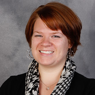 Emily Kimball, Assistant Professor for the Theatre Department, smiles against a gray background.