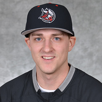 Danny Kneeland, Assistant Coach – Baseball/Facilities Support wearing a black baseball cap with a viking logo and a black jacket, smiling at the camera against a gray background.