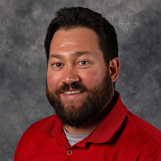 Jake Krier, Director of Alumni Relations for the Advancement Department, posed in front of a mottled gray background.