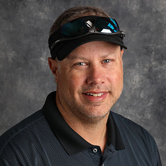 Matt Kuster, Chair of the Exercise Science Department, smiling against a gray textured background.