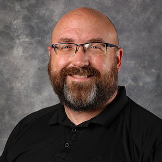 Patrick Langworthy, Housekeeping Technician for the Housekeeping Department, stands in front of a gray mottled background.