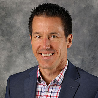 Jeffrey Lemke, Vice President of Admissions and Marketing for the Admissions Department, smiles in front of a gray textured background.