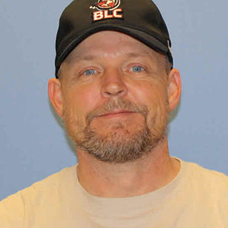 Greg Lieske, Maintenance Technician for the Maintenance Department, smiles subtly against a blue background.
