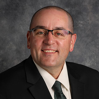 Jason Lowrey, Vice President and Adjunct Faculty for the Academic Affairs Department, smiling in front of a mottled gray background.