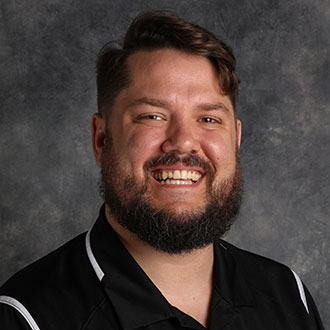 Aaron Mantey, Counselor of the Admissions Department, stands in front of a gray mottled background.