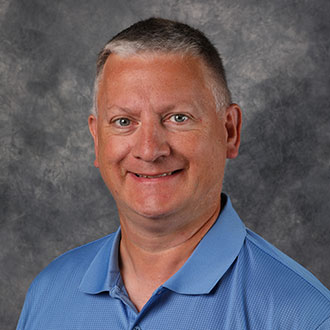 Director of Administrative Computing and Institutional Reporting for the Information Technology Services Department, stands in front of a gray textured backdrop.