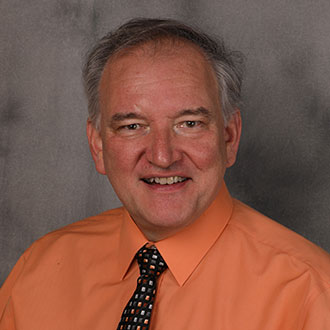 Dennis Marzolf, Adjunct Faculty of the Music Department, posed in front of a gray backdrop.