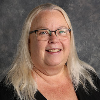 Deborah Matzke-Lewis, Director of the Nursing Department, stands in front of a gray textured background.